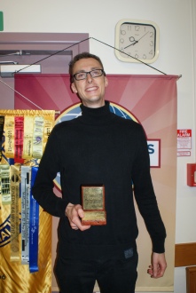 Timm holding the Toastmasters trophy for the evaluation contest with Toastmasters banners in the background